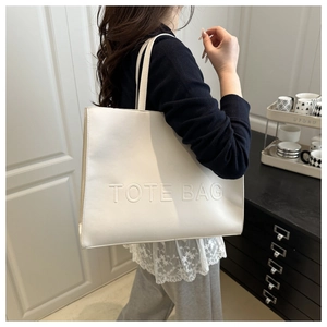 Detailed view of the large white tote bag with embossed letters on a model shoulder