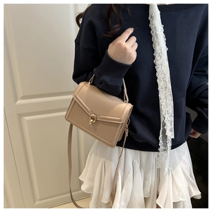 Detail of a beige leather handbag featuring a golden swivel metal lock and fine stitching