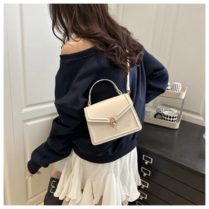 Mannequin portant un sac carré crème avec fermoir en U doré dans un décor chic