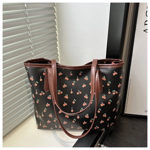 Detail of cherry print pattern on black tote bag with brown leather handles and piping