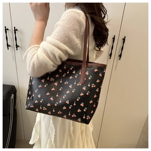 Detail of cherry print tote bag with brown leather straps shown on a shoulder