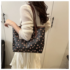 Close-up of stylish black tote bag with red cherry prints and brown shoulder straps