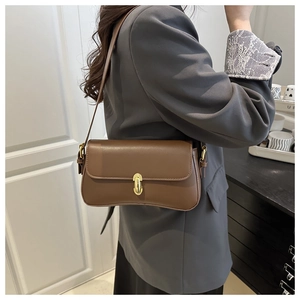 Close-up of caramel leather underarm bag featuring a refined gold oval clasp on the flap