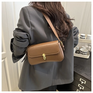 Gros plan d'un sac baguette rétro marron avec fermoir tournant doré sur un blazer gris