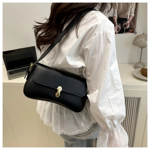Close-up of black leather underarm bag featuring a stylish gold buckle on a model