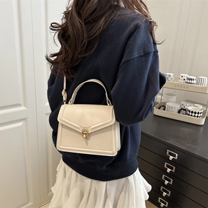 Sac à main minimaliste en cuir blanc crème avec fermoir doré porté par un modèle