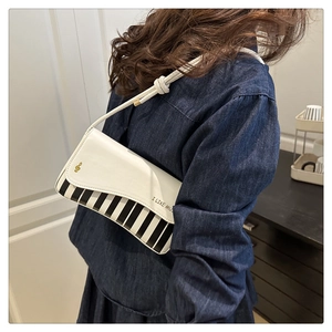 Detail of white piano-themed handbag with musical note charm and I LIKE MUSIC print