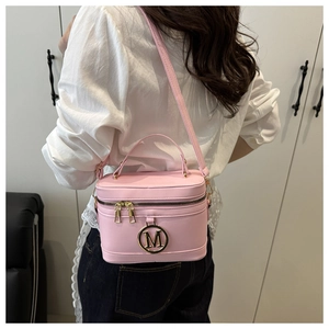 Sac bandoulière rose en similicuir avec détail M doré sur une tenue blanche élégante