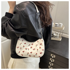 Close-up of a white cherry print shoulder bag with a silver chain strap worn by a model