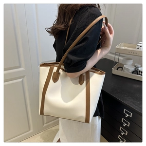 Detail of minimalist cream tote bag with brown trim worn by a model in home setting