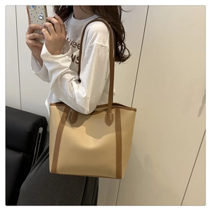 Side view of a large two-tone faux leather tote bag with long handles on a shoulder