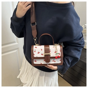 Detail of white handbag with cherry print and brown leather trim on a model