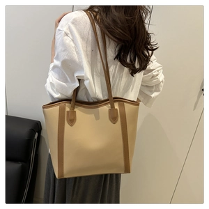 Detail view of large beige tote bag with brown leather trim worn by model