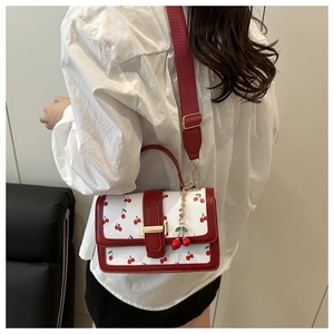 Detailed close-up of a white leather crossbody bag with red cherry prints and golden clasp