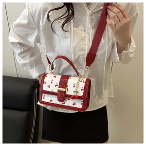 Detail view of white crossbody bag with cherry print, red wide strap and gold buckle