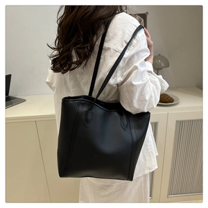 Detail of a large black matte leather tote bag worn by a model in a minimal office setting