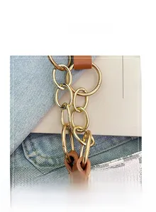 Detail of gold metal chain connector and brown leather strap on white checkered tote bag