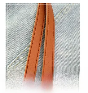 Close-up of brown textured leather strap with stitching on blue denim tote bag