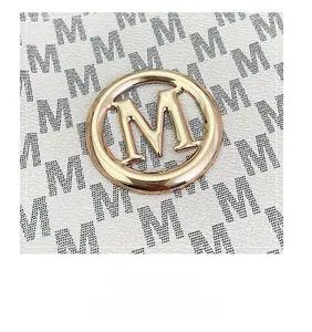 Macro view of gold M logo on white pebbled leather tote bag with black pattern