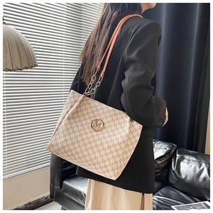 Detail of monogram printed tote bag featuring a gold M logo and orange chain strap