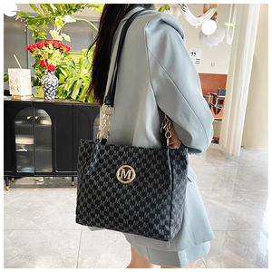 Detail of a large black tote bag with gray M pattern and gold logo on blue blazer