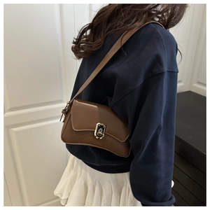 Dark brown leather underarm bag with gold metal buckle shown on a model's shoulder