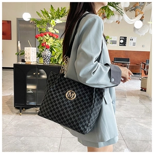 Detail of black tote bag featuring white M pattern and elegant gold metal logo