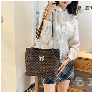 Close-up of brown tote bag featuring golden M logo and monogram patterned leather texture