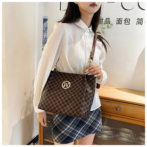 Detail of a brown monogram tote bag featuring a gold circular logo and leather straps