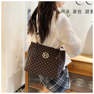 Detail of dark brown tote bag with M letter pattern and gold chain strap on shoulder