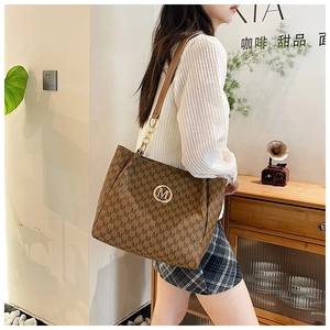 Detail of a dark brown monogram tote bag with gold chain strap and M-pattern design