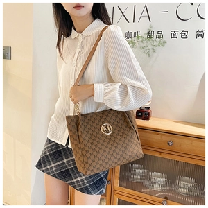 Detail of a brown tote bag with M-pattern print, gold logo, and leather chain strap