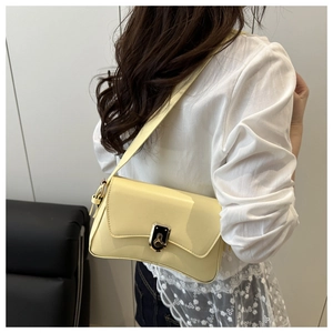 Detail of creamy yellow glossy leather shoulder bag with gold metal clasp on a model