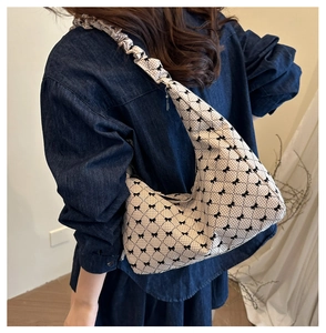 Detail of beige tote bag with black lattice pattern and pleated shoulder strap on model