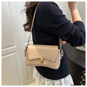 Detail of beige leather shoulder bag with gold clasp shown on a model in a casual setting