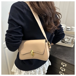 Detail of a beige leather baguette bag with a golden capsule clasp worn as a shoulder bag