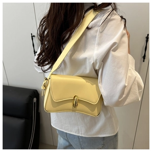 Detail of light yellow minimalist underarm bag featuring a cylindrical gold clasp and strap