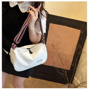 Detail of white canvas shoulder bag featuring a striped webbing strap and brand logo