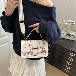 Crossbody white square bag with red cherry print and golden clasp on a female model