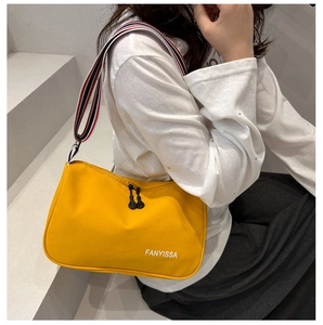 Detail of yellow canvas shoulder bag with striped strap and dual zipper closure
