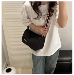 Detail of black cylinder bag with striped wide strap worn over a white casual T-shirt