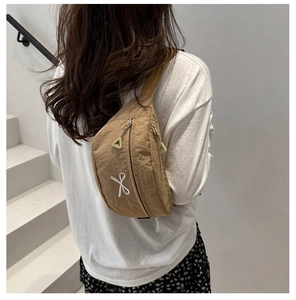 Detail of earthy nylon crossbody bag with geometric embroidery and green zipper pull