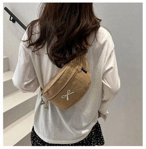 Detail of khaki nylon chest bag featuring a white bow and triangle metal zipper head