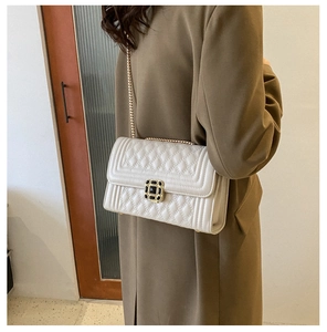 Detail of beige quilted shoulder bag featuring gold chain strap and black metal lock
