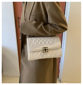 Detail of cream quilted crossbody bag featuring gold chain strap and black gem buckle