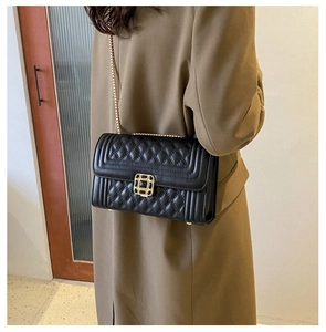 Detail of black quilted leather crossbody bag with vintage gold hardware on brown coat