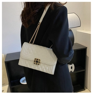 Close-up of white quilted handbag featuring a black-gold gemstone clasp and chain strap