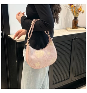 Pink floral print crescent moon bag worn by a model in a minimal indoor setting