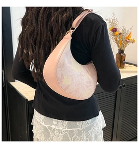 Detail showing pink crescent bag with floral print and gold metal hardware on a model