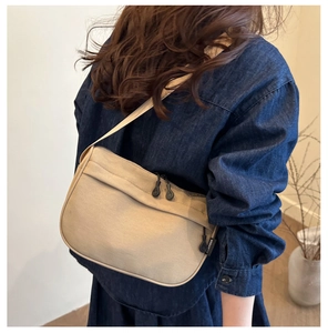 Detail shot of the beige canvas crossbody bag's adjustable strap and side brand tag